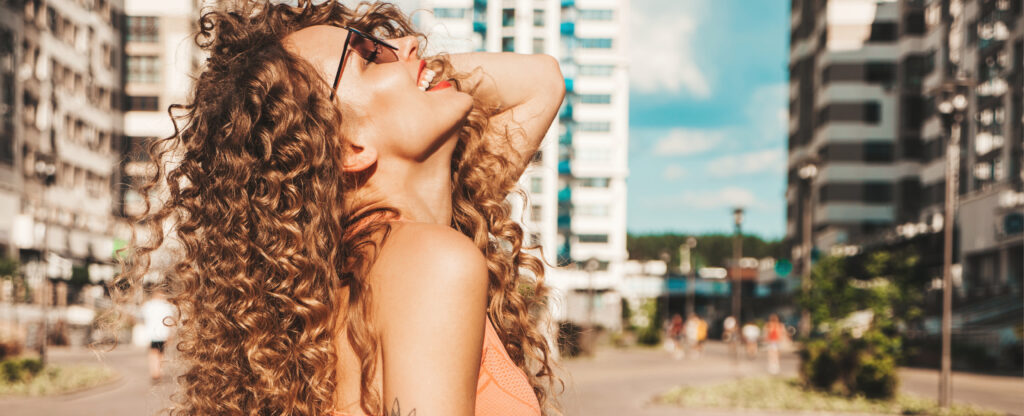 portrait of beautiful smiling model with afro curls hairstyle dressed in summer hipster clothes.sexy carefree girl posing in the street background. trendy funny and positive woman having fun