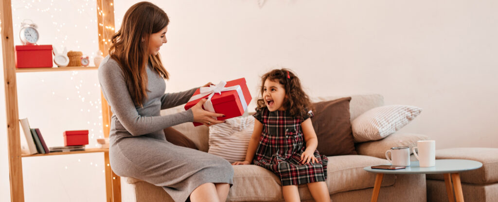 young woman giving present to daughter. mother and child posing with gift in holiday